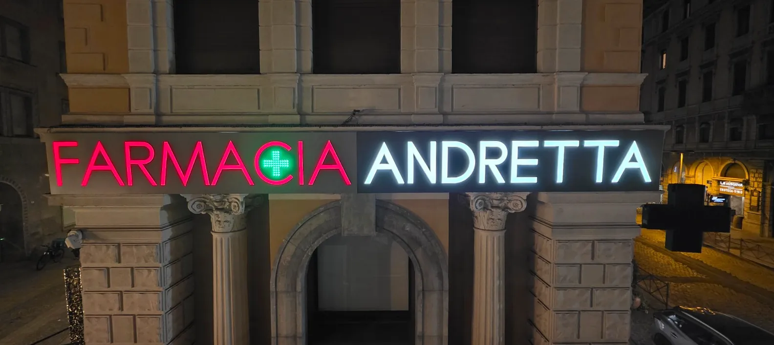 Insegna luminosa Farmacia Andretta di sera, con lettere LED rosse e bianche e croce verde