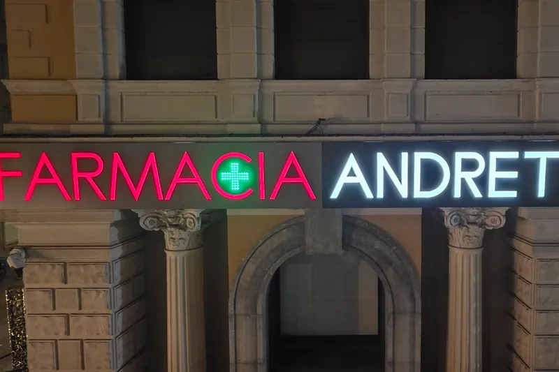 Insegna luminosa FARMACIA ANDRETTA con la croce verde, di sera