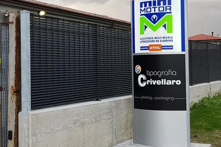 Totem con le insegne MINI MOTOR e tipografia Crivellaro davanti a un cancello